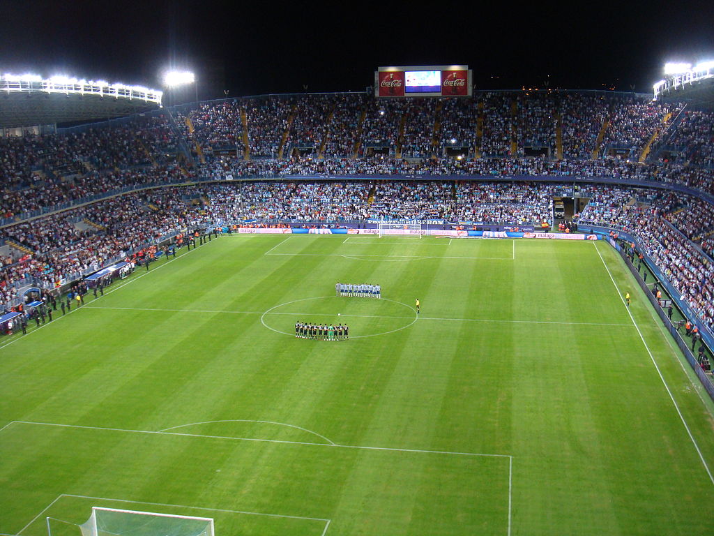 La Rosaleda Stadium with fans in the stands and aerial view of the pitch where two team are standing. 