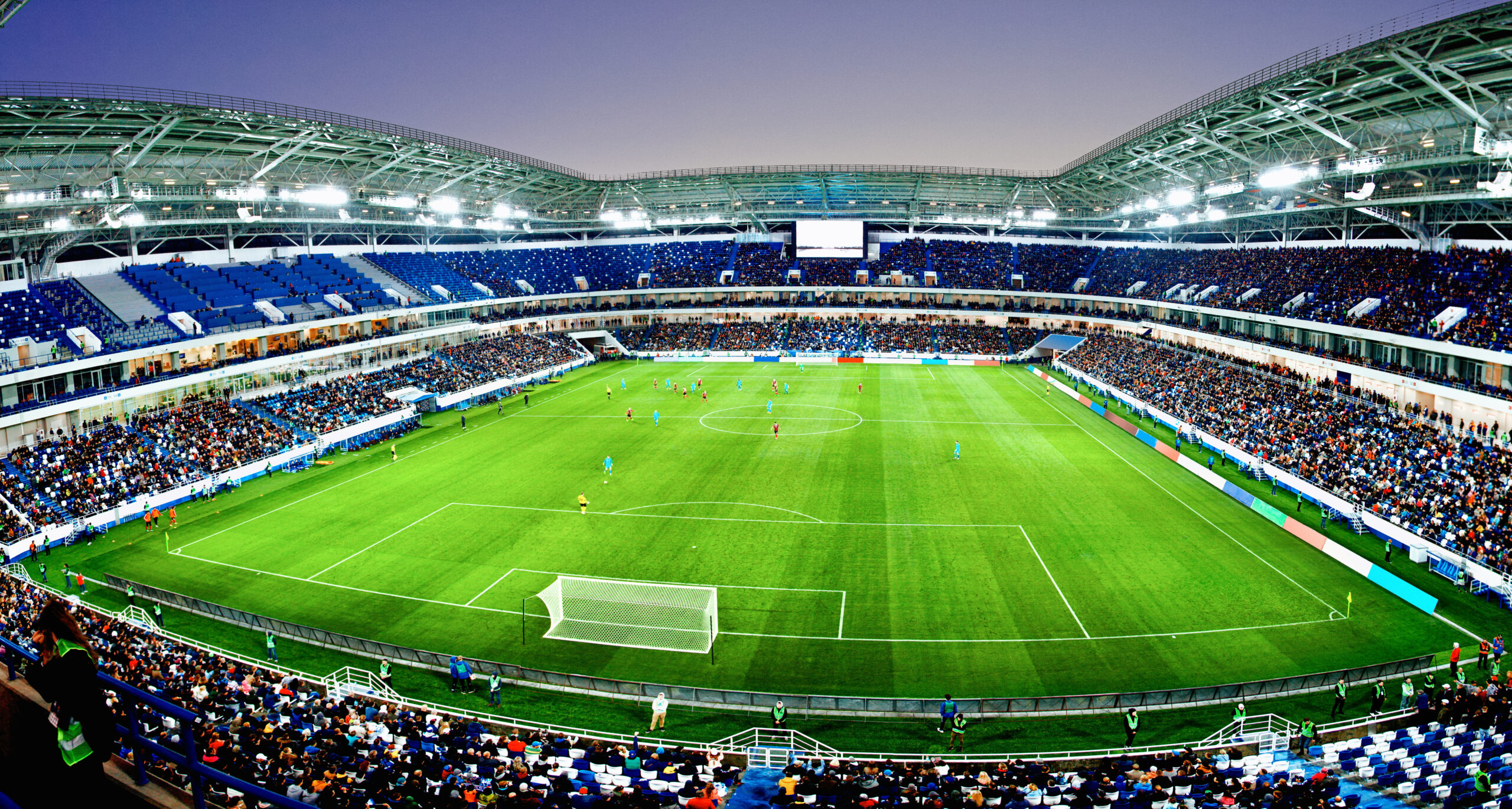 soccer (football) stadium pitch with ongoing match and fans cheering