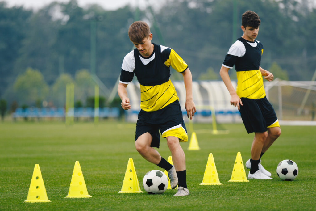 Young players dribble ball between training cones