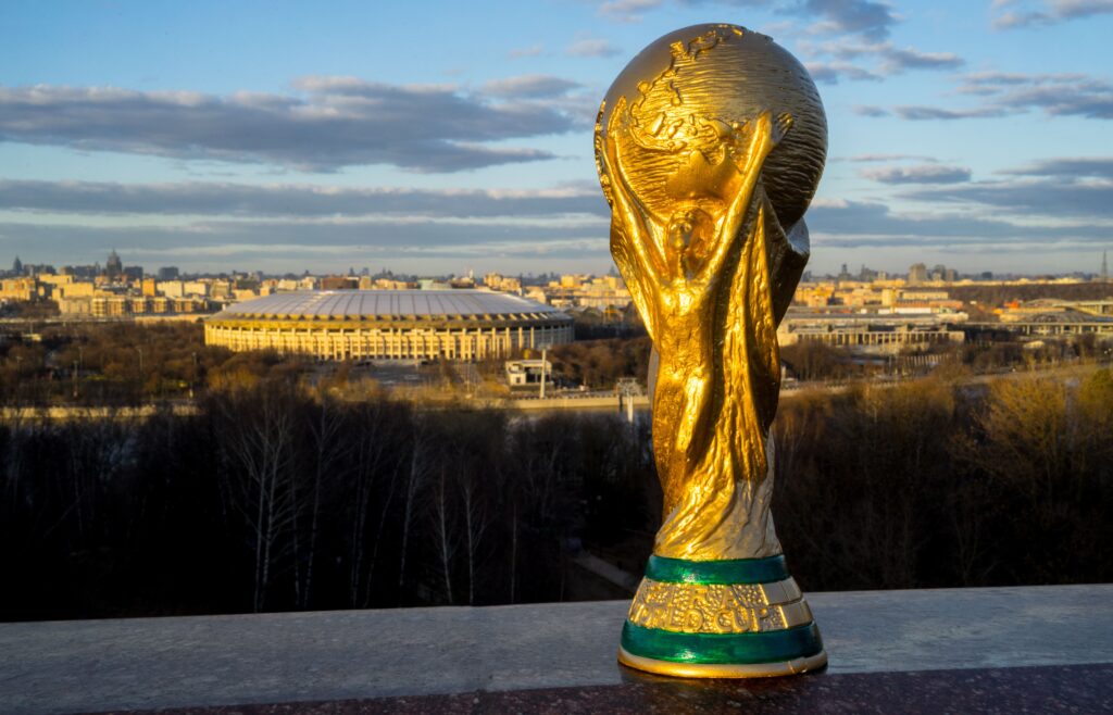 FIFA World Cup trophy with Luzhniki Stadium and Moscow’s skyline in the background at sunset.