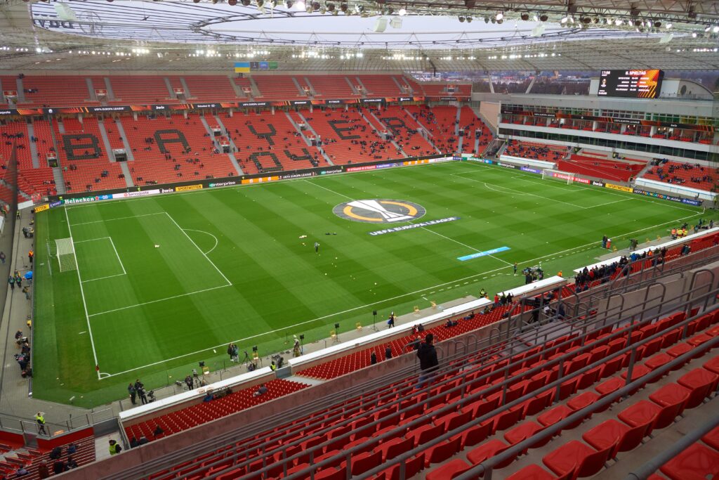 BayArena prepared for a UEFA Europa League match, with players warming up on the pitch and fans arriving in the stands.