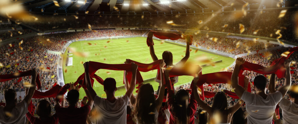 Sport match. Back view of football, soccer fans cheering their team with colorful scarfs at crowded stadium at evening time. Concept of sport, cup, world, team, event, competition