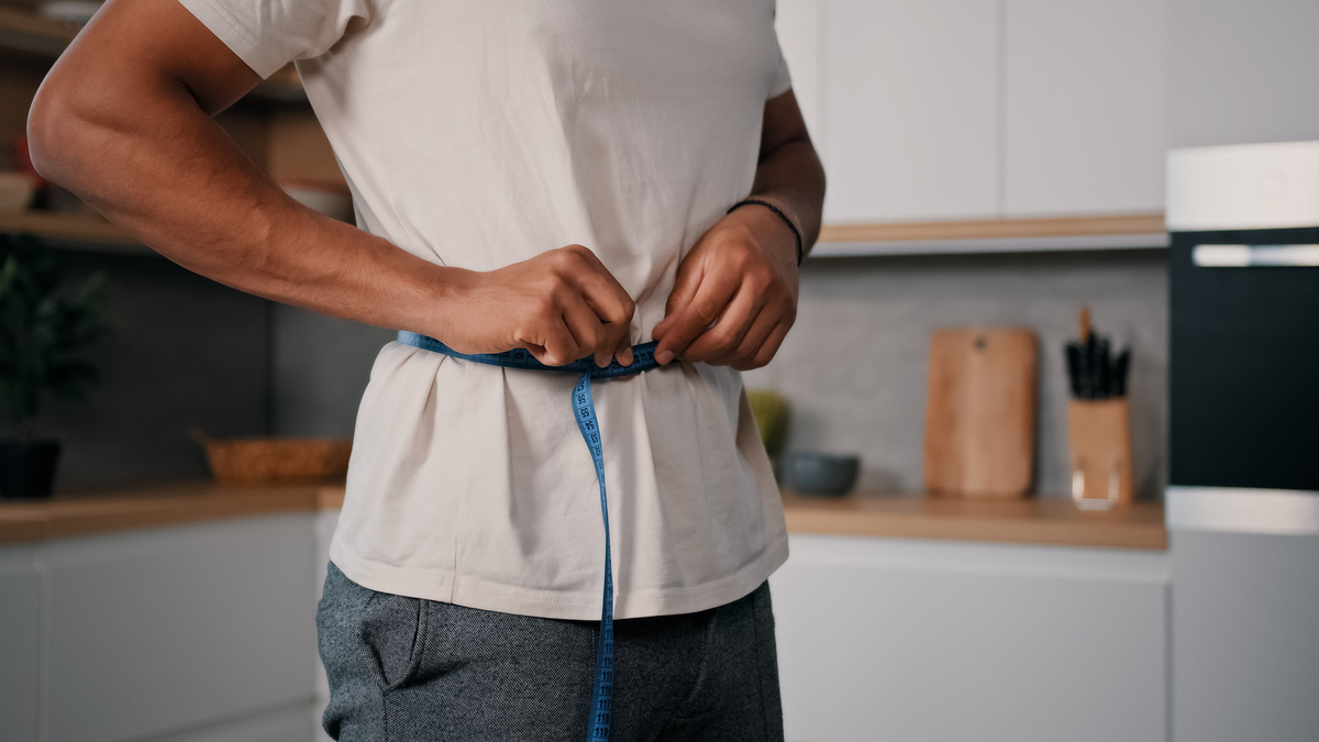 Guy measures waist with measuring tape