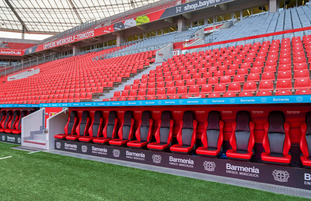 Team dugout at BayArena, featuring red and black seats with a view of the pitch.