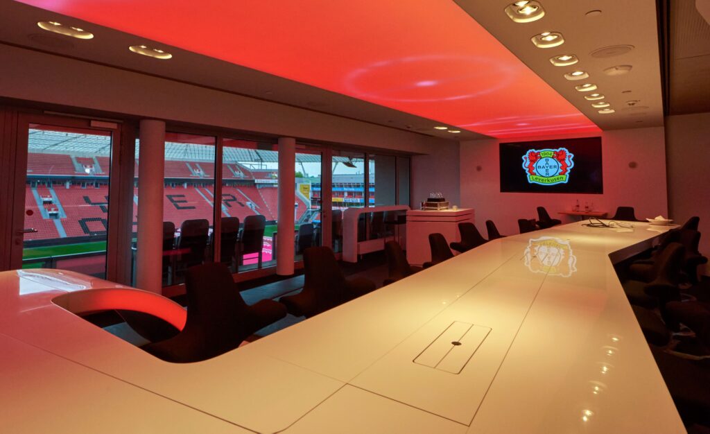 VIP lounge at BayArena with a modern design, red ceiling lighting, and a direct view of the stadium.