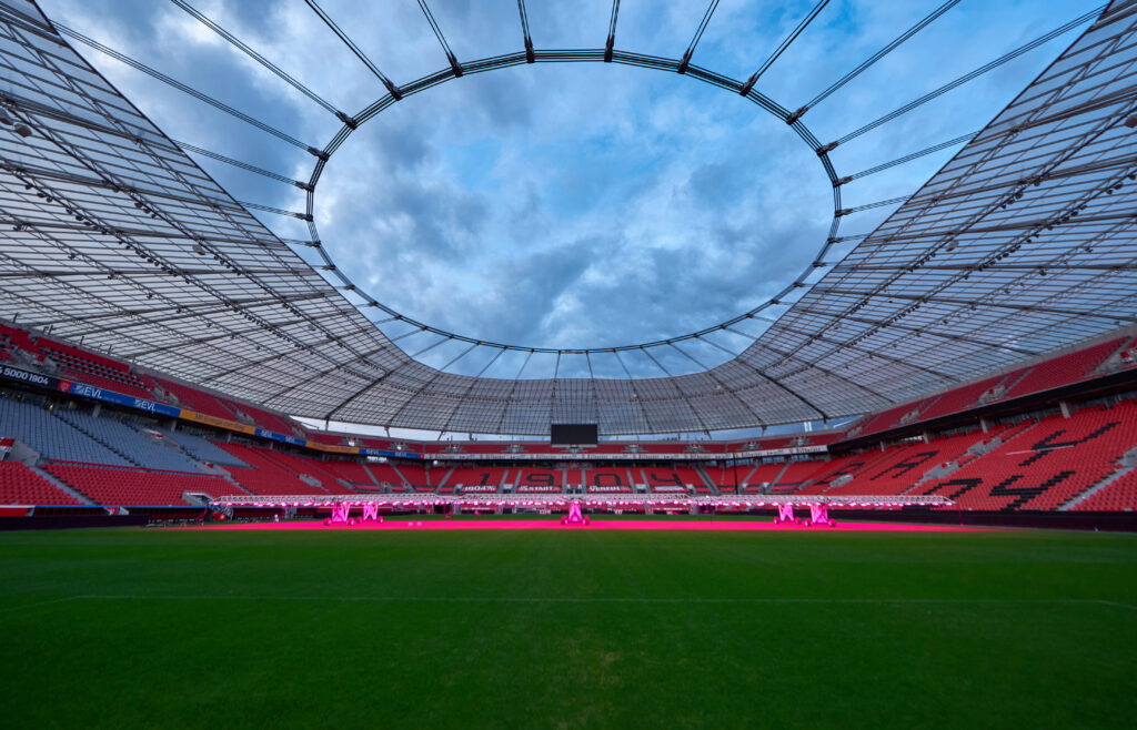 BayArena's interior at dusk, featuring its iconic circular roof and pitch lighting in operation.