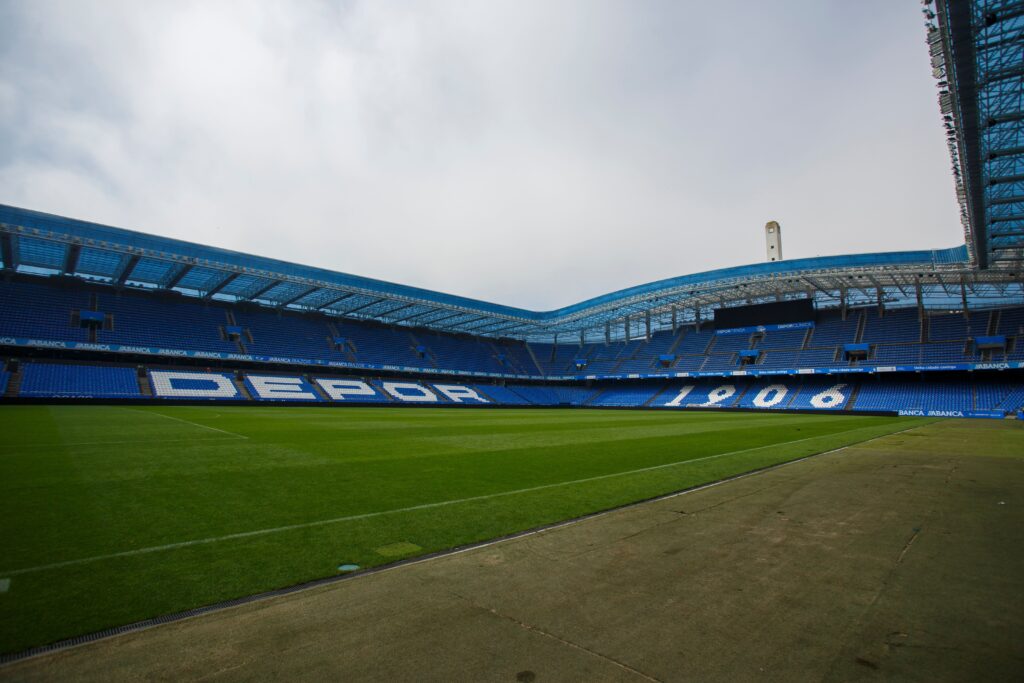 Riazor Stadium, home of Deportivo La Coruña, featuring blue seating and the club's founding year, 1906, displayed in the stands.