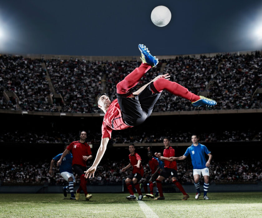 Football player kicking ball mid-air on field