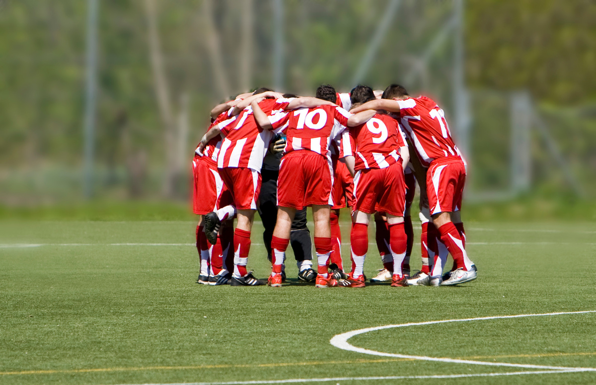 Soccer team of players in red shirts grouped up on the pitch