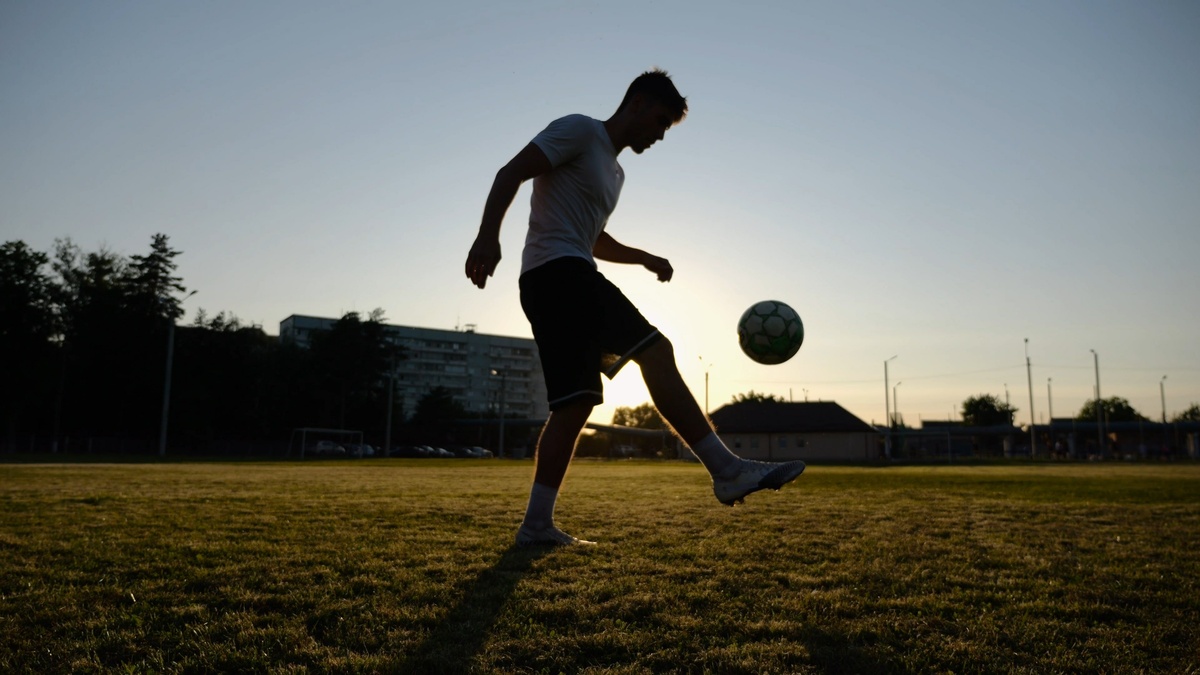 footballer juggling soccer ball on the field at sunset