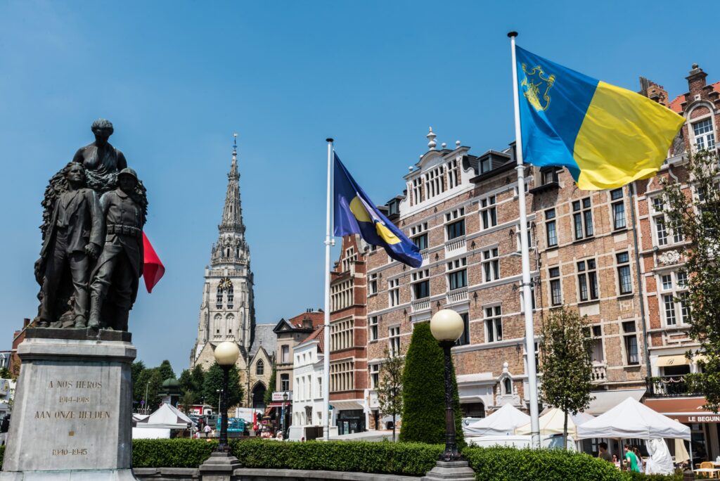 City square with a war memorial, historic buildings, and blue-yellow flags waving in the wind.