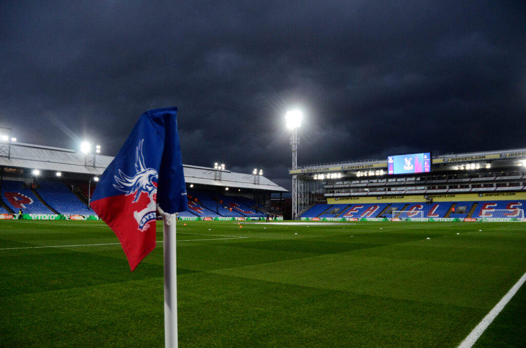 Selhurst Park under stadium lights, featuring a Crystal Palace corner flag and dark stormy skies.