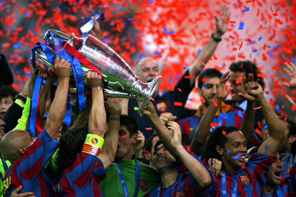 Jogadores do Barcelona comemoram a conquista do troféu da UEFA Champions League, erguendo-o alto em meio a uma chuva de confetes vermelhos e azuis.