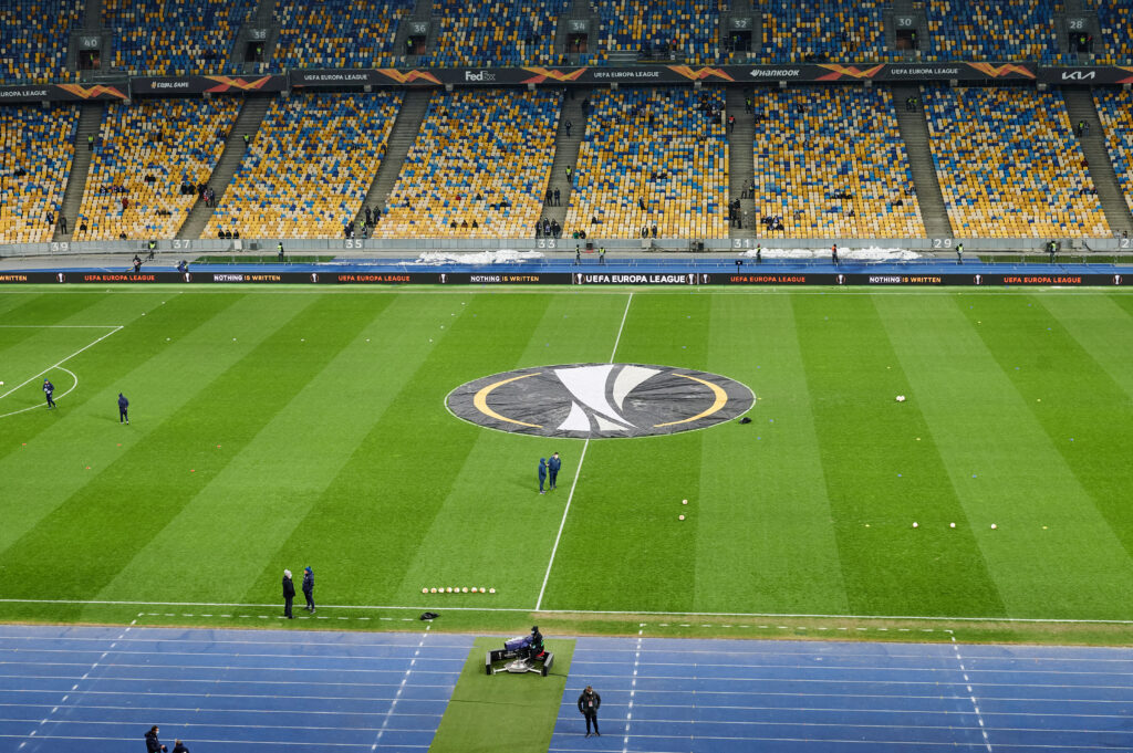 Vista de um estádio de futebol preparado para uma partida da UEFA Europa League, com o logotipo exibido no centro do campo. 