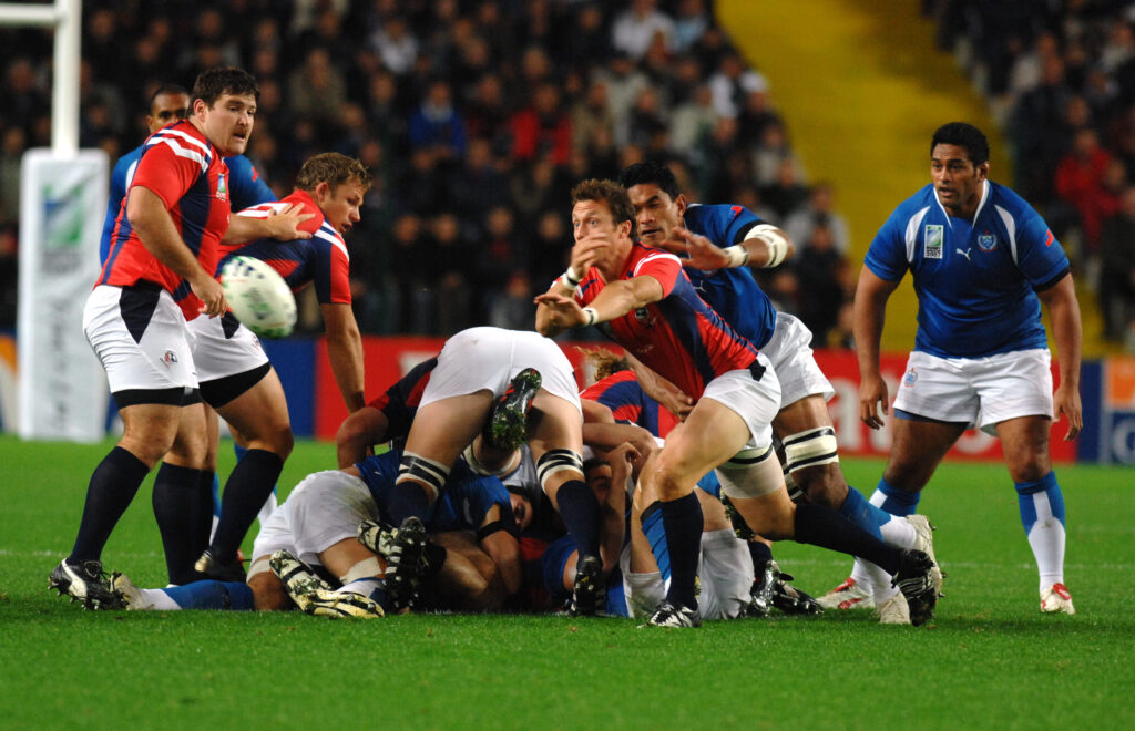 Rugby match action with players in red and blue jerseys competing for the ball.