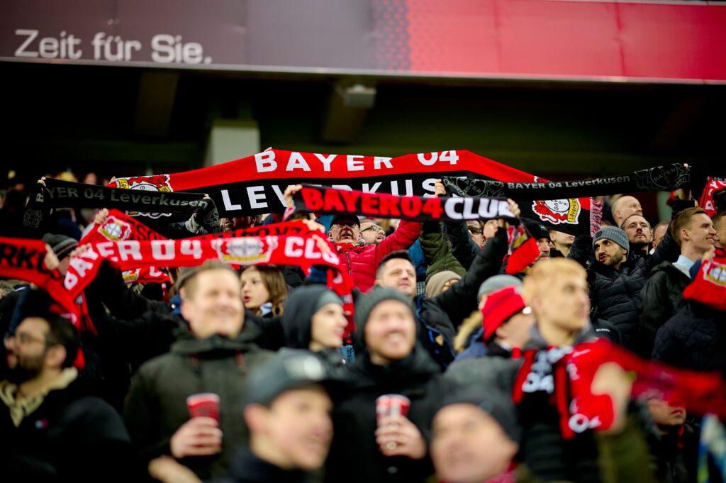 Bayer Leverkusen fans passionately supporting their team, holding up scarves in the stands.