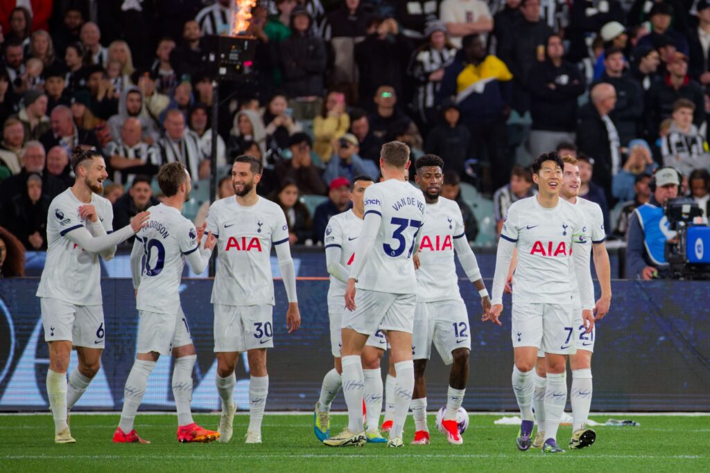 Jogadores do Tottenham Hotspur comemoram juntos no campo durante uma partida, vestindo seus icônicos uniformes brancos.