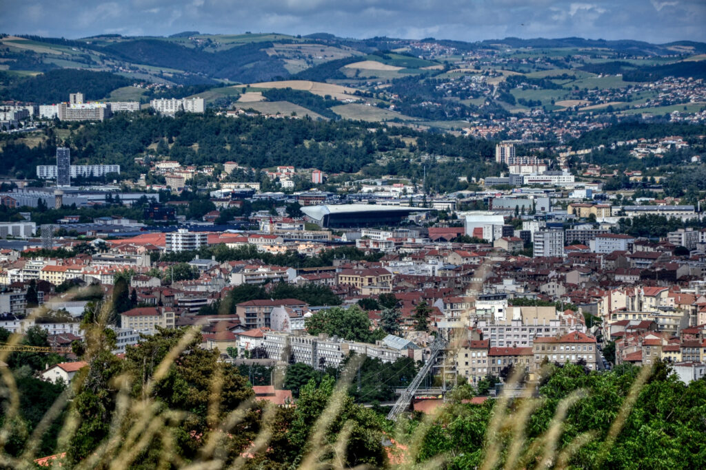 Panoramic view of a city with a stadium, surrounded by rolling green hills.