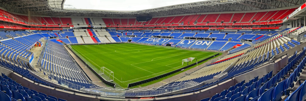 Uma vista ampla de um estádio de futebol moderno com assentos onde 'ONLY LYON' é exibido de forma proeminente, cercando um campo verde bem cuidado.