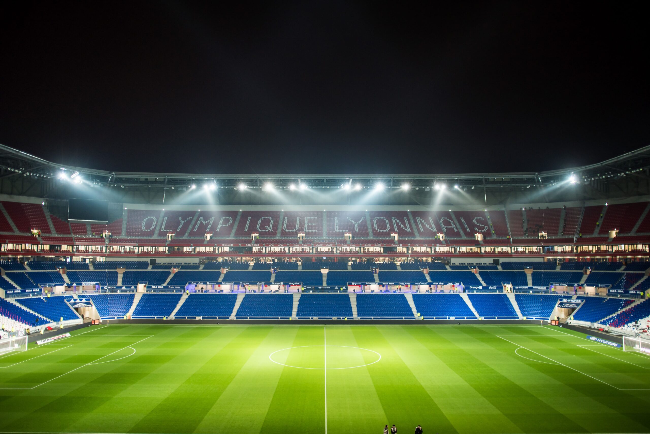 Uma vista noturna do estádio Olympique Lyonnais, brilhantemente iluminado com seu campo verde.