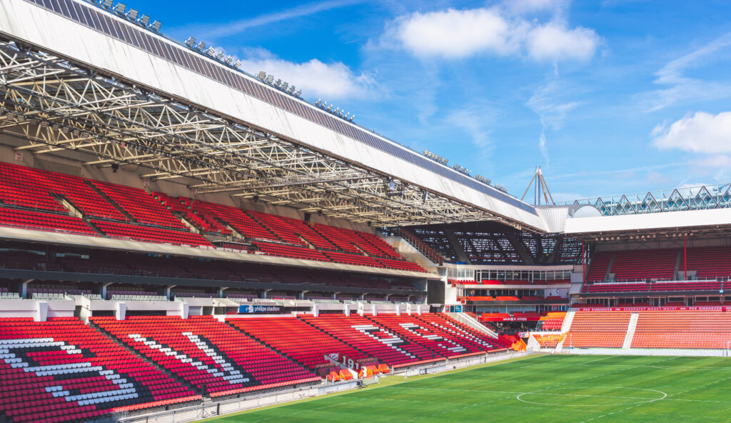 Philips Stadion, home of PSV Eindhoven, with red and white seating under a clear blue sky.