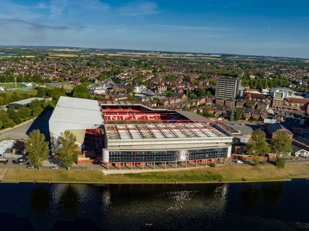 An aerial view of the City Ground stadium, home of Nottingham Forest FC, situated along the River Trent in Nottingham, England, on a sunny day.