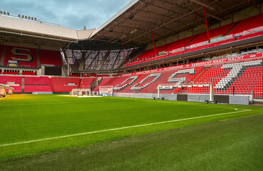 Philips Stadion, home of PSV Eindhoven, showcasing a lush green pitch, red and white seating, and artificial grow lights enhancing the grass.