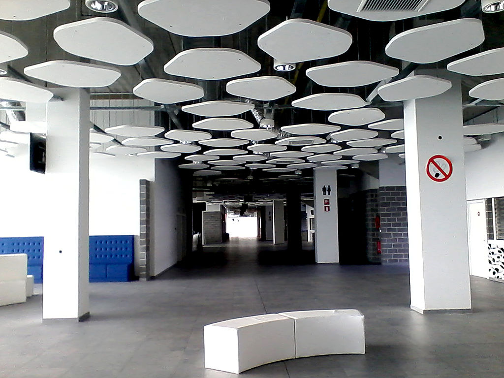 Interior of the Ghelamco Arena in Ghent, Belgium, featuring modern design with white geometric ceiling panels, minimalist seating, and a spacious hallway.