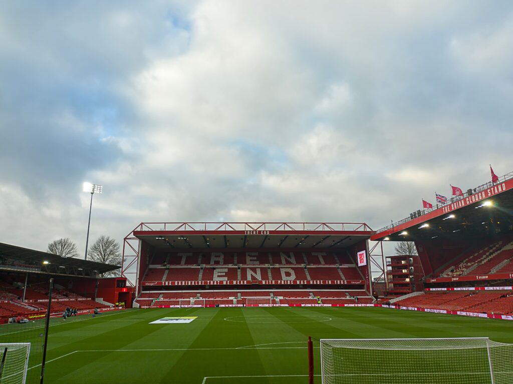 An inside view of the City Ground stadium, home of Nottingham Forest FC, showing the Trent End stand under a cloudy sky.