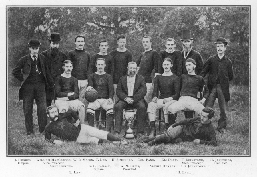 A historic black-and-white photograph of the Aston Villa football team, featuring players and club officials posing with a trophy, dressed in vintage football attire and formal wear.