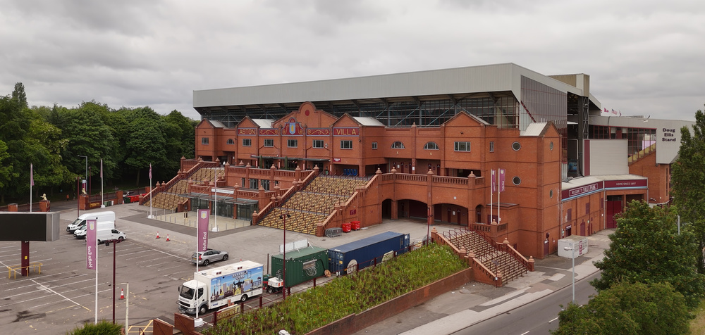 Exterior view of Villa Park stadium in Birmingham, home of Aston Villa, featuring its historic red-brick facade, staircases, and entrance area under an overcast sky.